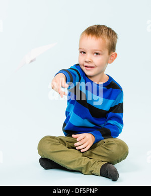 Happy boy playing with paper airplane in studio, fond bleu clair Banque D'Images