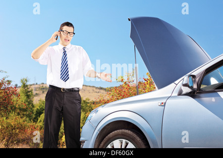 Jeune homme debout près d'une voiture cassée et de parler sur un téléphone, on a sunny day Banque D'Images