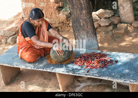 Femme indienne piment rouge séché de concassage de poudre avec une pierre ronde dans un village de l'Inde rurale. L'Andhra Pradesh, Inde Banque D'Images