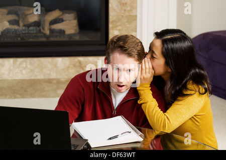 Photo de couple d'âge mûr, avec femme chuchotant à l'oreille de l'homme qui est sous le choc, tout en travaillant de chez vous. Banque D'Images