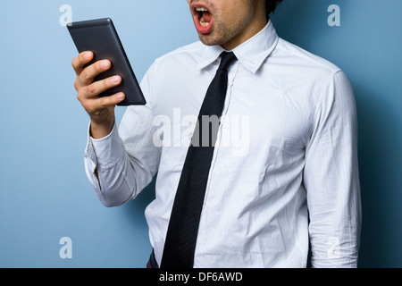 Jeune homme d'affaires est surpris par ce qu'il est en train de lire sur sa tablette numérique Banque D'Images