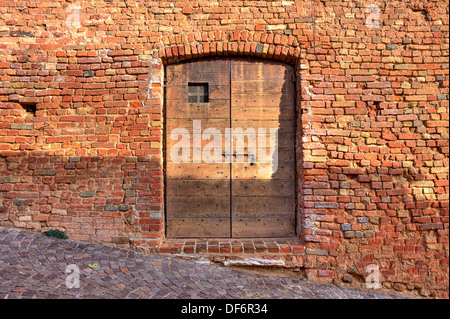 Rouge brique mur extérieur de maison ancienne de porte en bois sur la rue pavée dans petite ville italienne. Banque D'Images