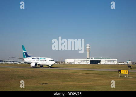 Boeing 737 de Westjet sur la piste en face de leur hangar et la tour de contrôle à l'Aéroport International de Calgary Banque D'Images