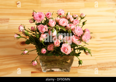 Bouquet de petites roses roses dans un vase en verre sur une table en bois. Banque D'Images