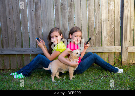 Soeur jumelle de jeunes filles, jouant avec le smartphone et chihuahua chien assis sur l'arrière-cour Banque D'Images