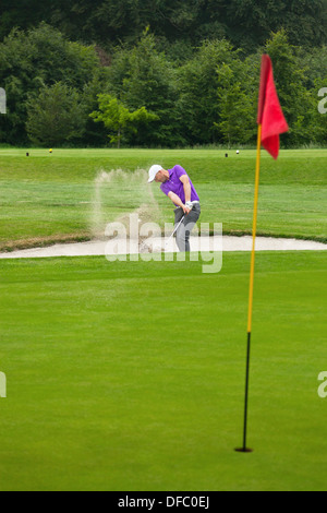 Un golfeur professionnel frapper sa balle d'un bunker avec le sable et la balle en l'air. Banque D'Images