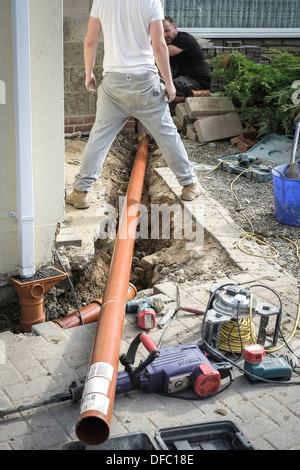 Deux constructeurs portant un tuyau de drainage dans une tranchée. Banque D'Images
