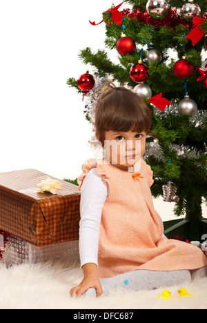 Cute little girl sitting near Christmas Tree with presents Banque D'Images