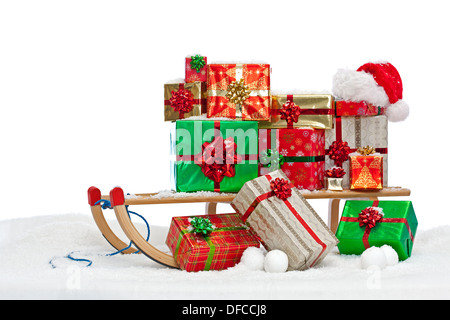 Un traîneau chargé avec gift wrapped Christmas presents et un chapeau de Père Noël, assis sur la neige sur un fond blanc. Banque D'Images