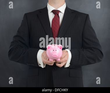 Homme en costume holding a piggy bank sur fond gris Banque D'Images