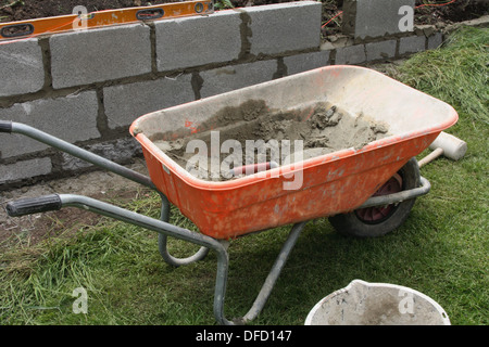 Un mur est construit, une brouette pleine de ciment est à l'avant du mur. Banque D'Images