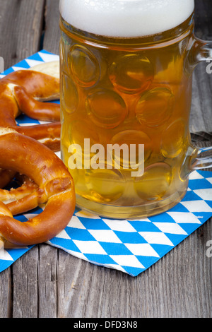 Une tasse de bière et des bretzels sur des serviettes avec losanges bleu et blanc sur une table en bois rustique Banque D'Images