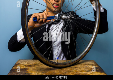 Jeune homme d'affaires tente de réparer une roue de bicyclette Banque D'Images