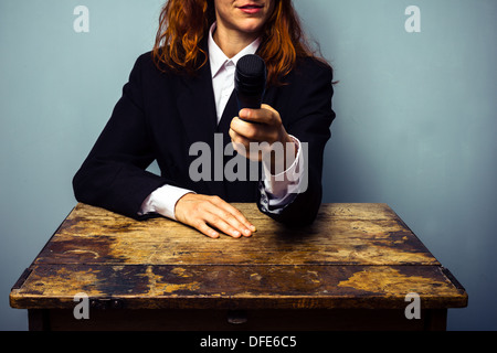 Jeune femme en costume est assis à un bureau et pointant un micro à l'appareil photo Banque D'Images