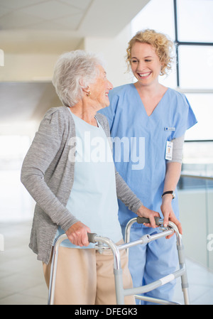 Senior patient avec walker smiling at nurse in hospital corridor Banque D'Images