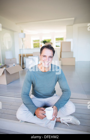 Portrait of smiling man drinking coffee parmi les boîtes de carton Banque D'Images