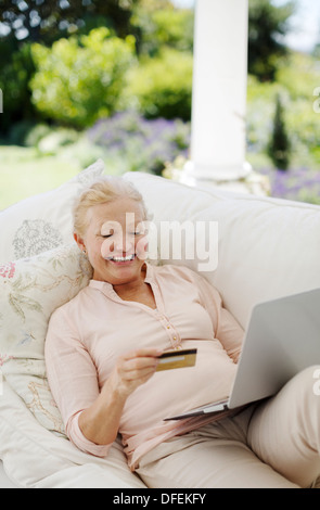Senior woman shopping online on patio sofa Banque D'Images