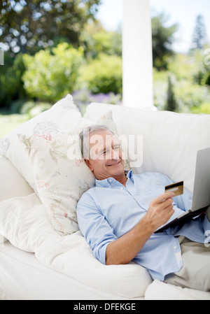 Man shopping online on patio sofa Banque D'Images