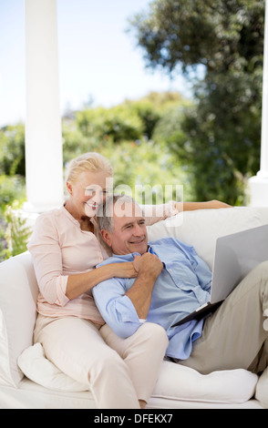 Couple using laptop on patio sofa Banque D'Images