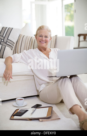 Senior woman using laptop on plancher du salon Banque D'Images