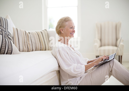 Senior woman using laptop on plancher du salon Banque D'Images