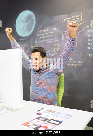 Businessman cheering at desk in office Banque D'Images