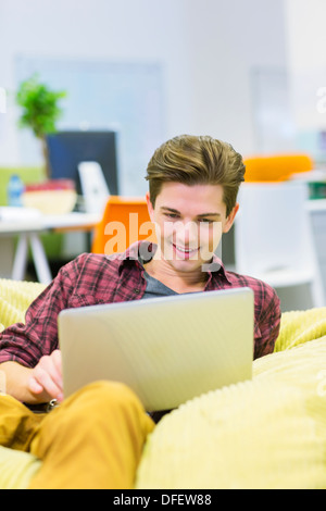 Businessman using laptop in chaise de sac d'haricot dans office Banque D'Images