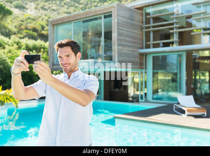 Man taking self-portrait with camera phone at poolside Banque D'Images