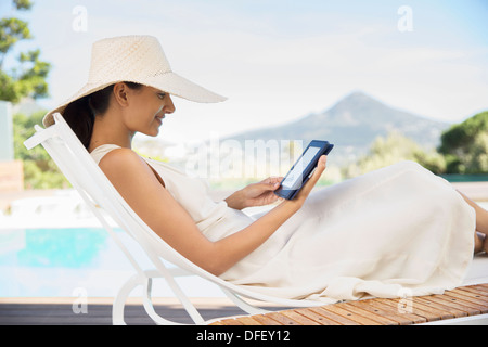 Woman using digital tablet on lounge chair at poolside Banque D'Images