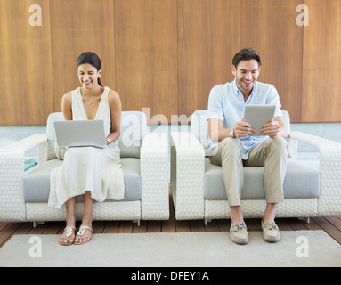 Couple à l'aide d'ordinateur portable et tablette numérique dans les fauteuils Banque D'Images