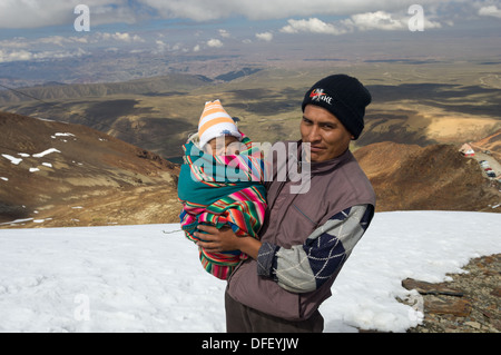 Père bolivien portant son enfant nouveau-né à la 5421 m (17 785 ft) Sommet du Chacaltaya comme une tradition locale, montrant les restes de la le glacier de Chacaltaya, près de La Paz, Bolivie Banque D'Images