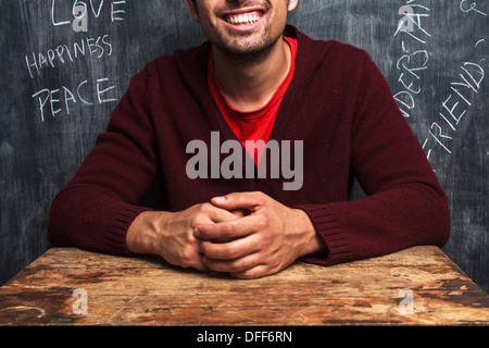 Heureux jeune homme est assis en face de tableau noir avec écrit dessus des mots positifs Banque D'Images