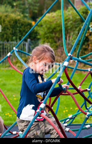 Petite fille de grimper une corde d'Escalade à une aire de jeux pour enfants Banque D'Images