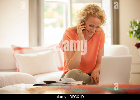 Woman talking on cell phone and using laptop in living room Banque D'Images