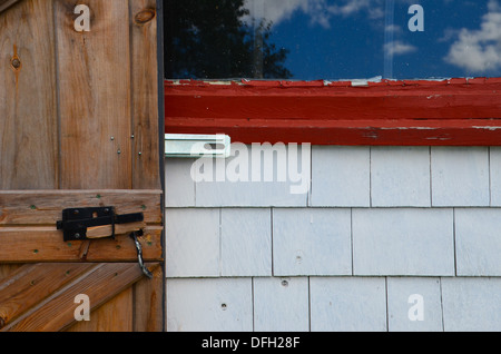 Moyenne géométrique photo d'une porte de grange en bois brun contre white barn bardeaux, châssis de fenêtre rouge et un ciel bleu, la réflexion de la fenêtre Banque D'Images