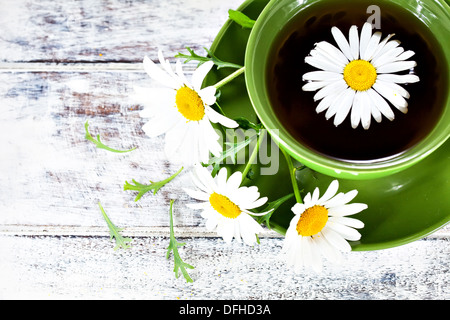 Libre d'une tasse de thé de camomille avec des herbes médicinales servi en tasse en céramique verte et quelques fleurs sauvages sur la surface en bois laqué blanc Banque D'Images