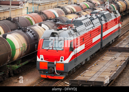 Locomotive diesel-électrique moderne rouge se déplace sur des rails de chemin de fer avec les entraîneurs de fret Banque D'Images