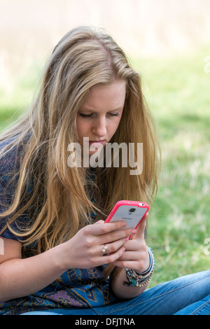 Jeune fille, l'ADOLESCENT DE DIX-SEPT,texto sur téléphone mobile à l'extérieur /CELLULE Banque D'Images