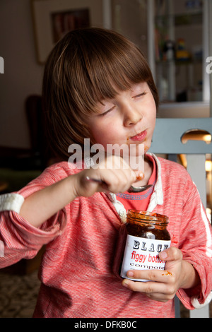 Quatre ans et demi ans bénéficiant d'un pot de compote de figues. Banque D'Images