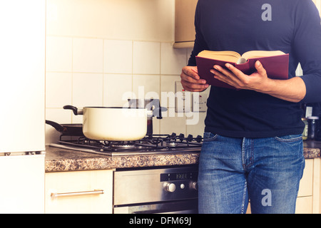 Jeune homme avec livre à cuisinière dans la cuisine Banque D'Images