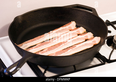 Quatre bandes de bacon non cuit dans un 12' Heavy Cast Iron Skillet sur poêle à gaz Banque D'Images