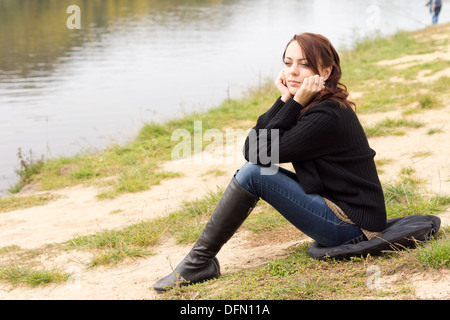 Mode belle jeune femme assise sur un coussin sur la rive d'apprécier la nature comme elle pose son menton sur ses mains de contentement. Banque D'Images