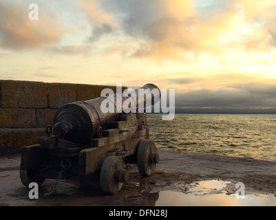 Vieux, rouillé cannon soulignant à la mer pendant un coucher de soleil sur la mer. Banque D'Images