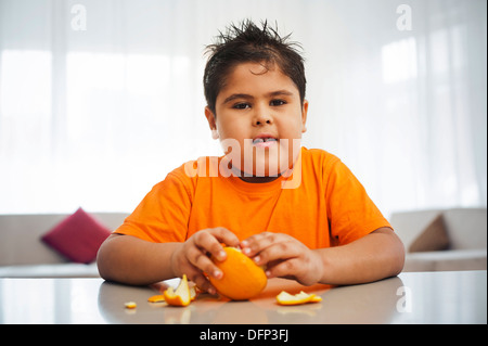 Garçon assis à une table une orange de déroulage Banque D'Images