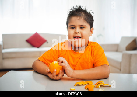 Garçon assis à une table une orange de déroulage Banque D'Images