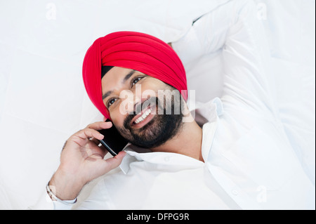 Smiling homme sikh couché sur le lit et talking on mobile phone Banque D'Images