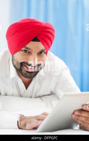 Homme Sikh à l'aide d'une tablette numérique et souriant Banque D'Images