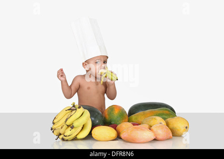 Un enfant de 3 ans portant des costumes chef et manger une banane. Banque D'Images