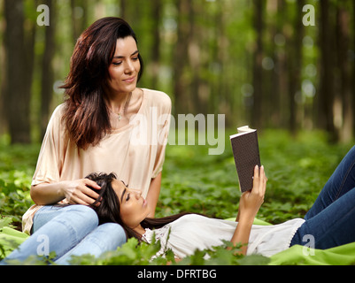 Mère et fille assis dans la forêt sur une couverture avec fille posant sa tête sur les genoux de sa mère lire ensemble Banque D'Images