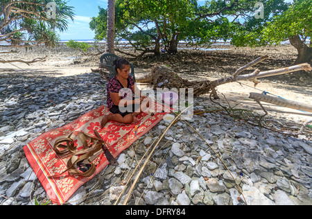 Femme de Kosrae est assis sur une natte près du bord de l'océan tandis qu'elle tisse des feuilles de palmier séchées et des obus sur des hangings de mur Banque D'Images